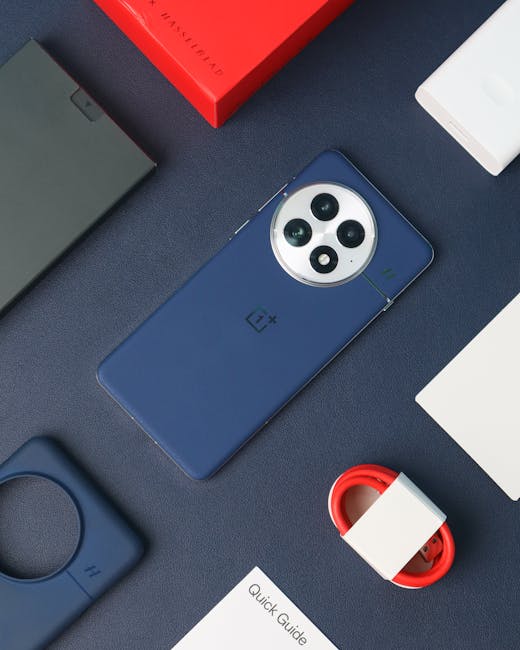 A close-up of a smartphone with a blue case and a prominent triple-lens camera on the back, placed on a dark textured surface along with other electronic accessories. Nearby, there is a small, circular device in a matching blue case, a white box, a red and white cable organizer, a white sheet of paper, and a partially visible red box. The arrangement appears organized and clean, with the surfaces showing no dust or smudges. The lighting is bright and even, highlighting the sleek finishes of the items. This setup reflects a tidy workspace focused on electronic devices and accessories, fitting within a modern, professional environment. The image is associated with Carpet Cleaning Putney, emphasizing the importance of surface cleanliness and maintenance, aligning with their expertise in domestic and commercial surface cleaning services, such as on Durnsford Road flats in SW15 Putney.